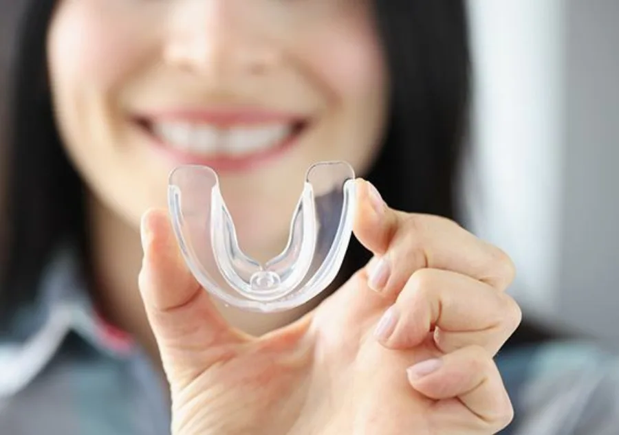 A blurred smiling woman holding a transparent mouthguard